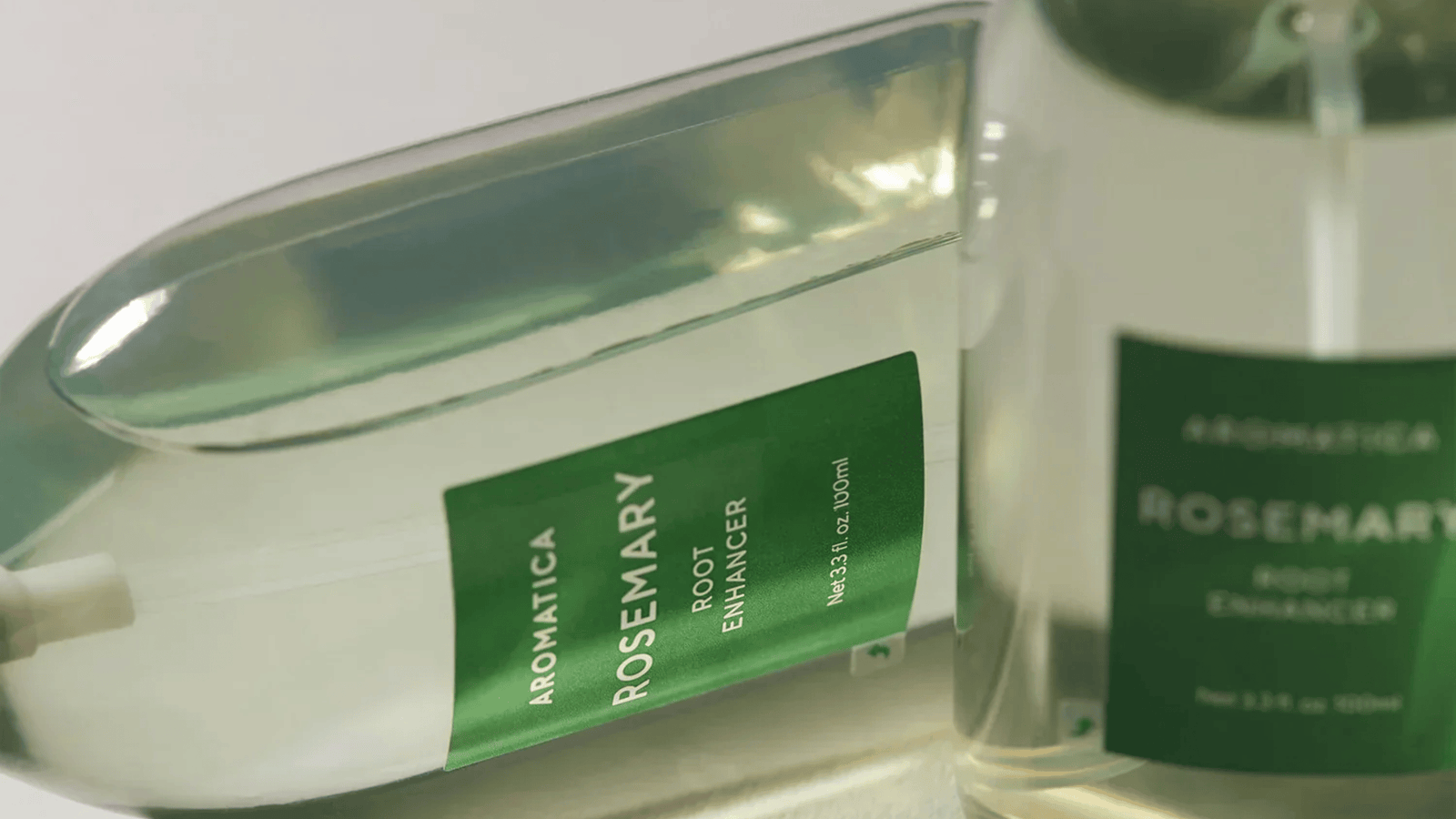 AROMATICA Rosemary Root Enhancer i transparent flaska med grön etikett och skyddskåpa. Närbild som framhäver produktens minimalistiska design och naturliga hårvårdskoncept.