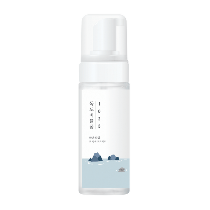 1025 Dokdo Bubble Foam" est un produit nettoyant pour le visage de ROUND LAB, emballé dans un flacon pompe blanc au design simple et épuré, orné de texte et d'illustrations minimalistes de paysages marins. 