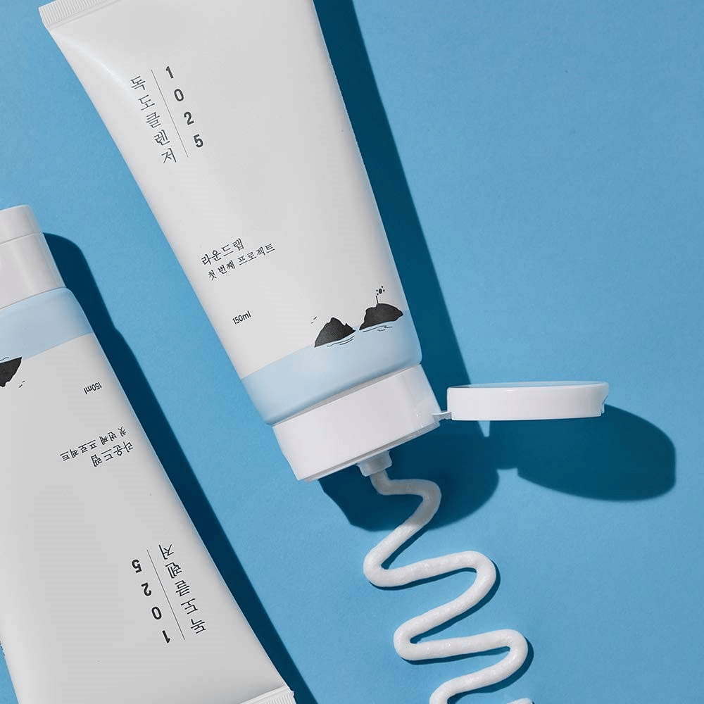 Deux tubes de 1025 Dokdo Cleanser sur fond bleu, dont un avec bouchon ouvert et un cordon ondulé de nettoyage pressé.