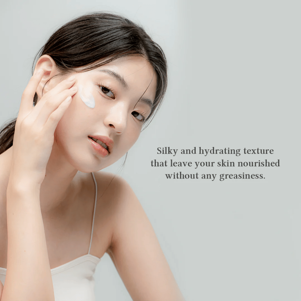 L'image montre une femme appliquant une crème pour le visage. Le texte sur l'image décrit le produit comme soyeux et hydratant, et souligne qu'il nourrit la peau sans laisser de sensation grasse. Cela suggère que la crème a une consistance légère et agréable qui est bien absorbée par la peau.