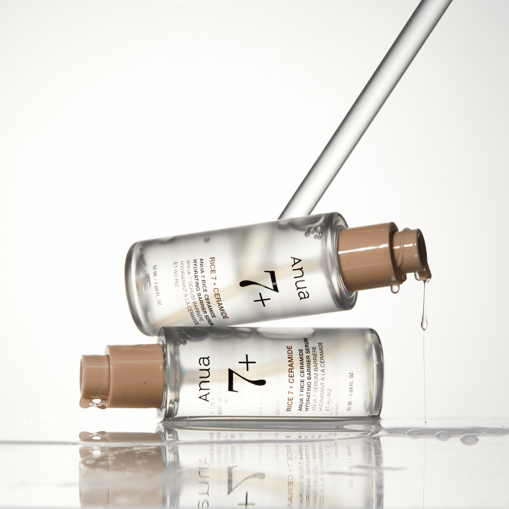 L'image montre deux bouteilles transparentes de "Anua 77 Rice + Ceramide Hydrating Barrier Serum" avec des gouttes coulant d'une pipette. Le sérum, enrichi de riz et de céramides, est conçu pour hydrater et renforcer la barrière cutanée. Les bouteilles sont élégamment conçues, ce qui renforce la sensation de produit haut de gamme.