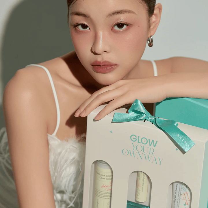 Mannequin avec un maquillage élégant tenant la boîte cadeau « Glow Your Own Way » de AXIS-Y – un Kit de soin de la peau élégant, parfait comme cadeau pour vous-même ou pour quelqu'un que vous appréciez.