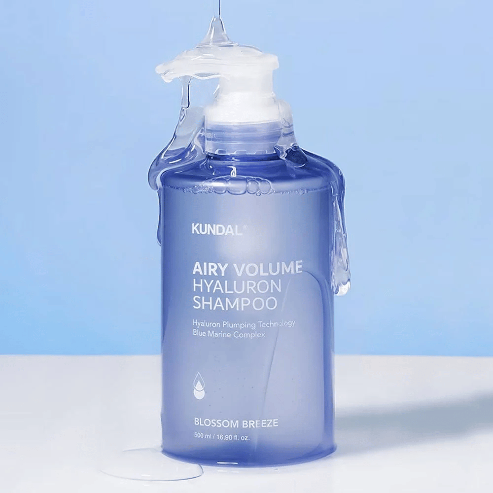 KUNDAL Airy Volume Hyaluron Shampoo Blossom Breeze dans un flacon pompe bleu, avec de l'acide hyaluronique et Blue Marine Complex, photographié avec de l'eau courante.