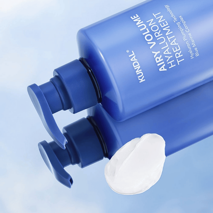 KUNDAL Airy Volume Hyaluron Treatment dans un flacon pompe bleu couché, avec un produit crème blanche visible à côté.