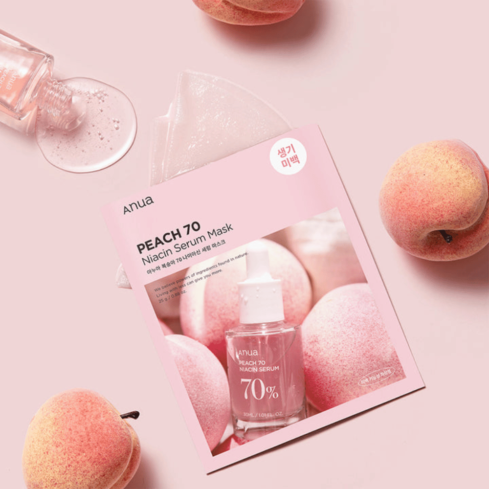 Une image de Anua PEACH 70 Niacin Serum Mask, entourée de pêches et d'un flacon de sérum. L'image a un fond rose doux, ce qui complète l'emballage rose et met en valeur le produit et les ingrédients.