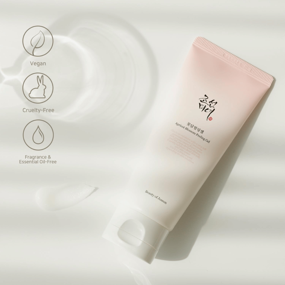 Un tube avec Apricot Blossom Peeling Gel repose sur une surface réfléchissante avec des icônes indiquant que le produit est vegan, respectueux des animaux et exempt de parfum et d'huiles essentielles.