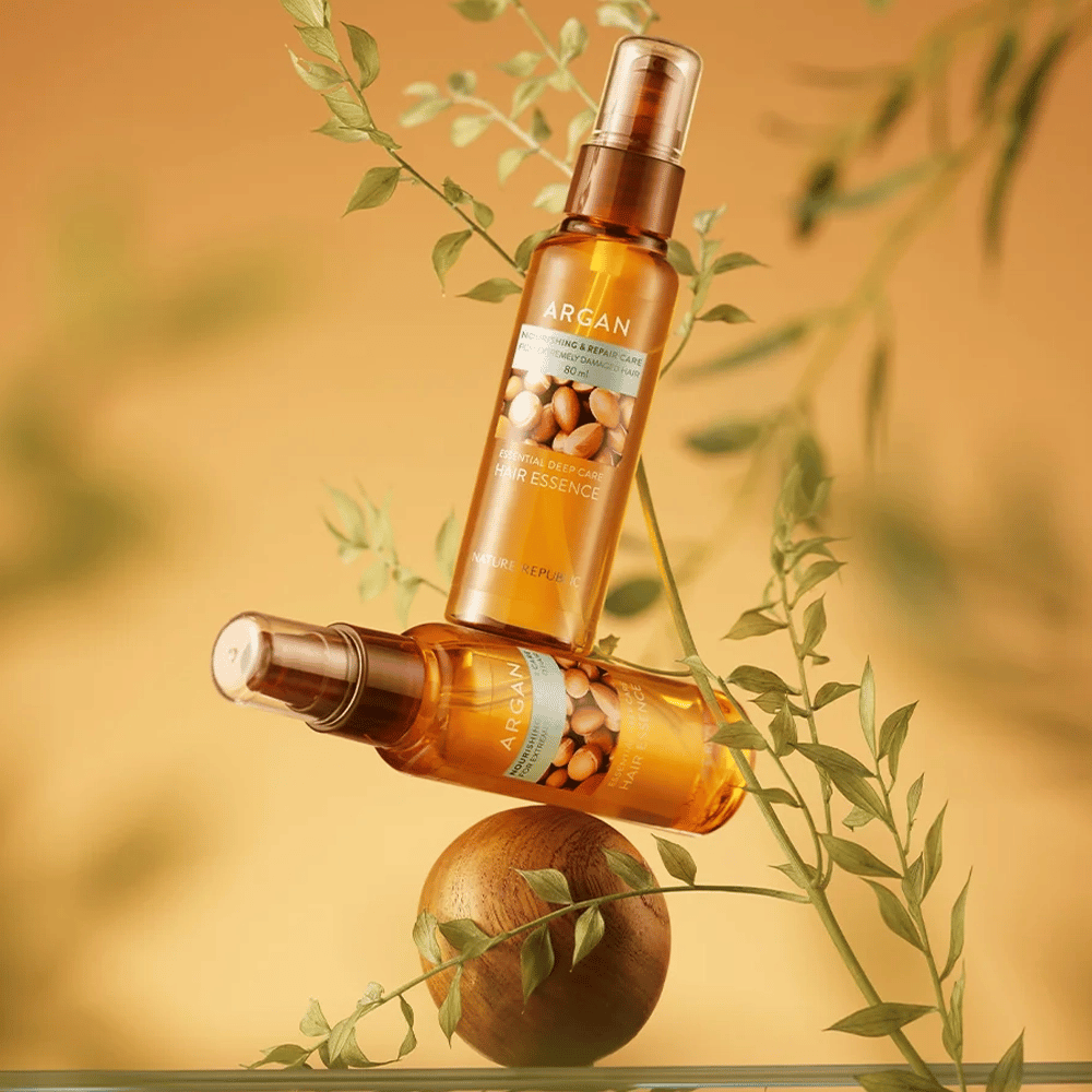 Deux bouteilles Nature Republic Argan Essential Moisture Hair Oil placées parmi des feuilles vertes – éclat soyeux pour cheveux secs.