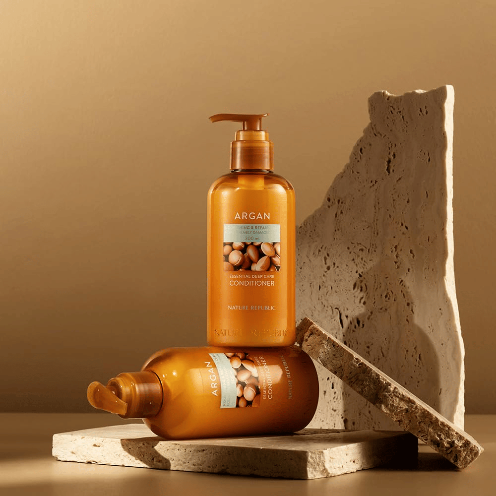 Deux bouteilles de Nature Republic Argan Essential Moisture Repairing Conditioner sur une surface en pierre de ton chaud.
