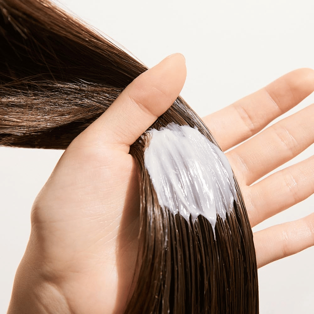 Une main applique Nature Republic Argan Essential Moisture Repairing Hair Mask sur cheveux mouillés – masque hydratant qui renforce et adoucit les cheveux.