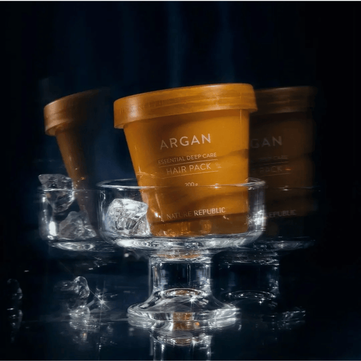 Nature Republic Argan Essential Moisture Repairing Hair Mask placé sur un plat en verre avec des glaçons – masque capillaire luxueux et nourrissant.