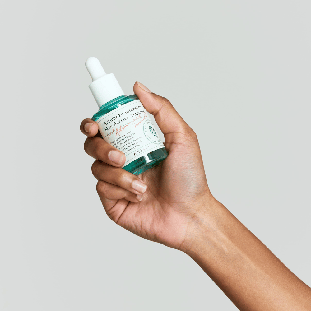 Une main tient une bouteille de sérum de soin de la peau avec l'étiquette "Artichoke Intensive Skin Barrier Ampoule.