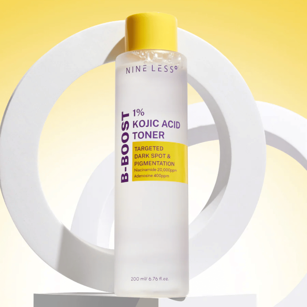 NINE LESS B-Boost 1% Kojic Acid Toner debout contre un fond jaune avec le texte "Targeted Dark Spot & Pigmentation". Tonique uniformisant le teint avec niacinamide et adénosine.