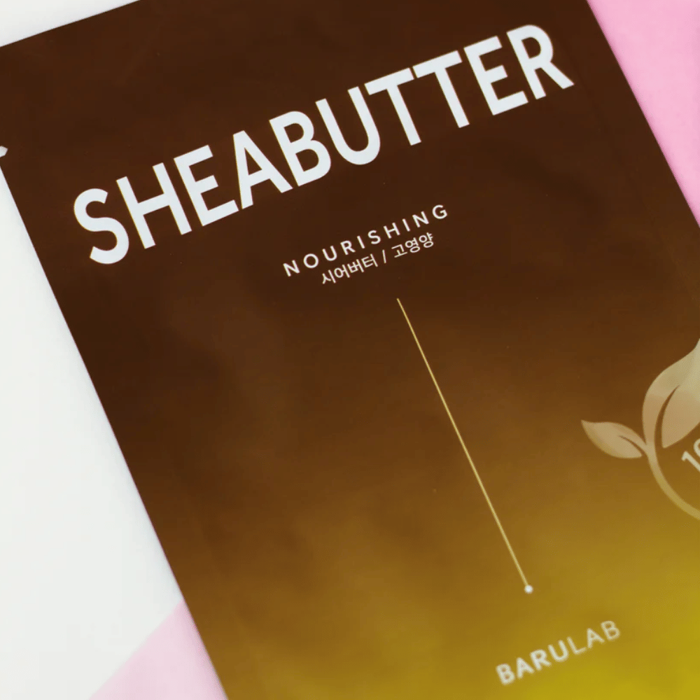 Un gros plan d'un emballage de masque "SHEABUTTER Nourishing" BARULAB. Le produit est marqué comme "Produit 100% Végan" et a un dégradé de couleur du brun foncé au brun clair.