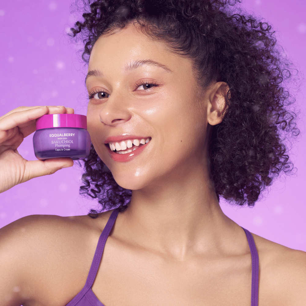 Femme avec une peau éclatante tenant EQQUALBERRY Bakuchiol Plumping Capsule Cream et souriant devant un fond violet.
