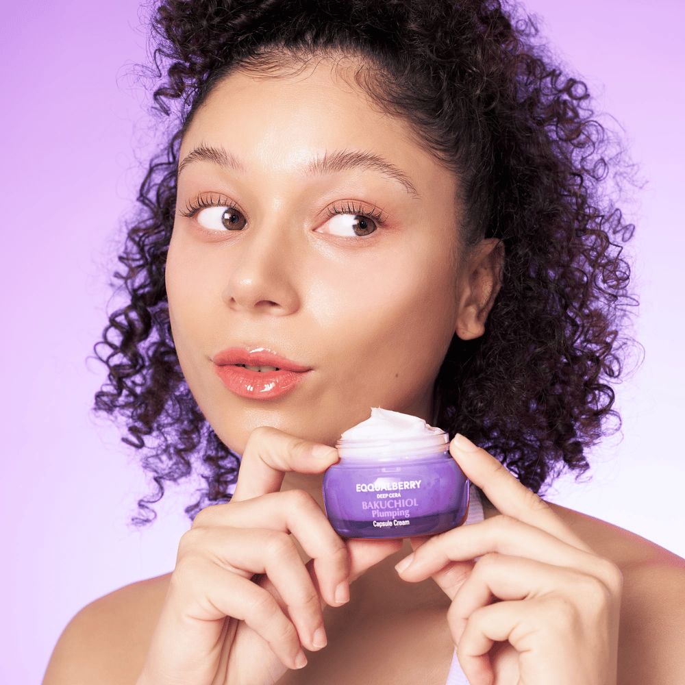 Femme tenant EQQUALBERRY Bakuchiol Plumping Capsule Cream dans la main et montrant sa peau hydratée et éclatante sur un fond violet.