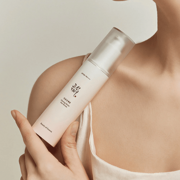 Une femme tenant une bouteille de Beauty of Joseon's Ginseng Moist Sun Serum SPF 50+ PA++++, offrant une protection SPF 50+ PA++++ et des bienfaits pour la peau.