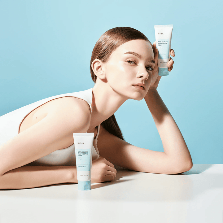 Image lifestyle où un modèle pose avec iUNIK Beta-Glucan Daily Moisture Cream sur un fond bleu clair. L’image transmet une sensation de propreté, de fraîcheur et d’hydratation tout en exposant clairement le produit.