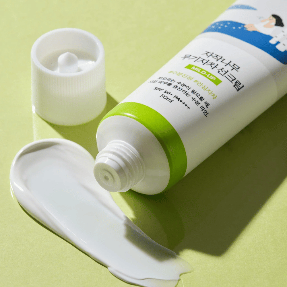 Gros plan sur Birch Juice Moisturizing Mild Up Sunscreen avec bouchon dévissé, crème solaire blanche étalée sur fond vert clair, SPF 50+ PA++++, 50 ml.