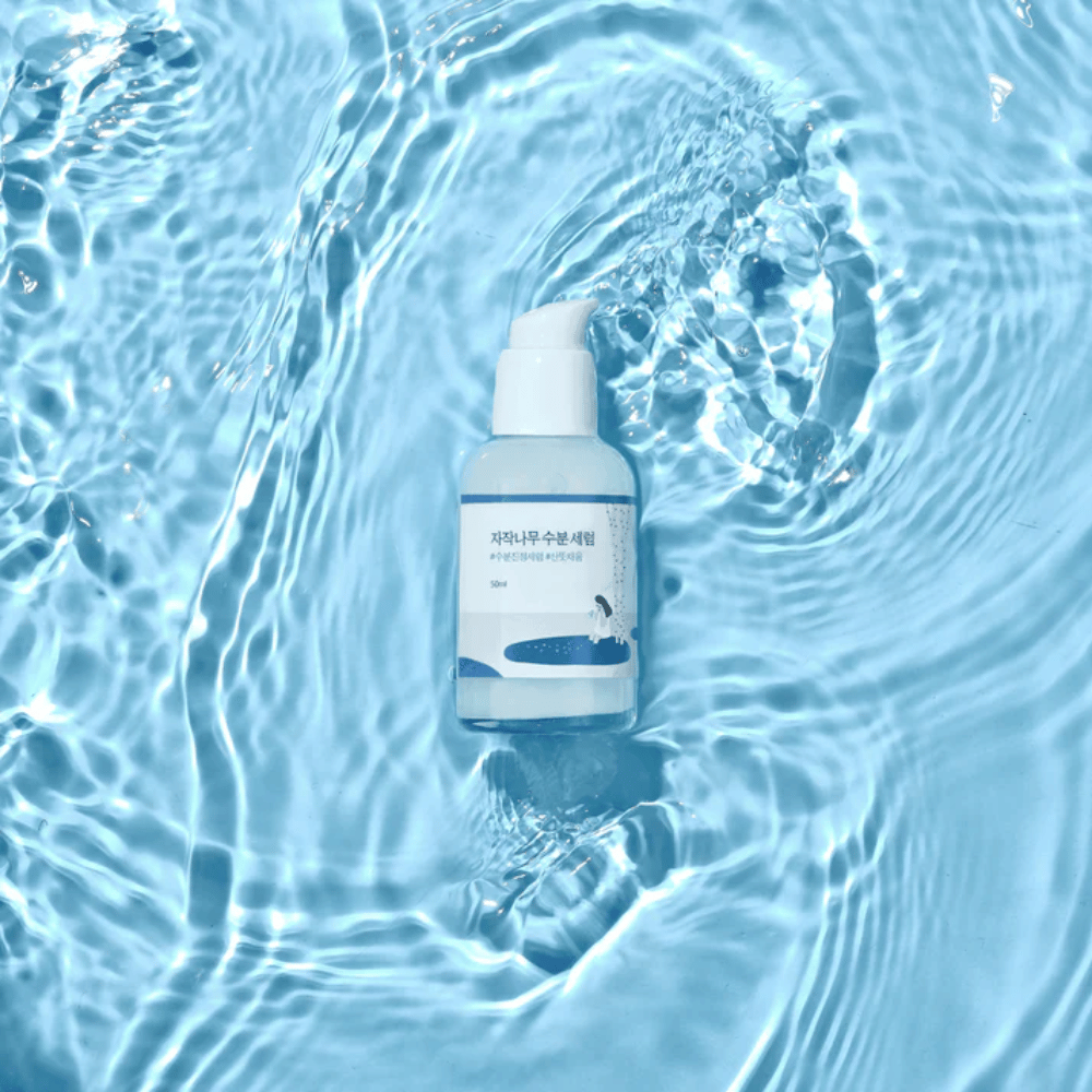 Round Lab Birch Juice Moisturizing Serum dans un flacon pompe flottant sur de l'eau bleue avec des reflets de soleil.