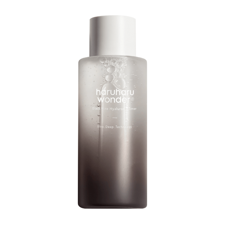 Une bouteille de haruharu wonder Black Rice Hyaluronic Toner avec un dégradé de couleur gris à blanc et des gouttes d'eau à la surface, sur un fond blanc.