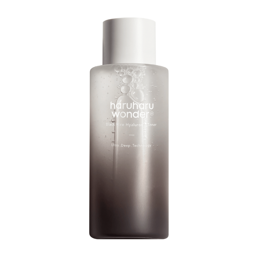 Une bouteille de haruharu wonder Black Rice Hyaluronic Toner avec un dégradé de couleur gris à blanc et des gouttes d'eau à la surface, sur un fond blanc.