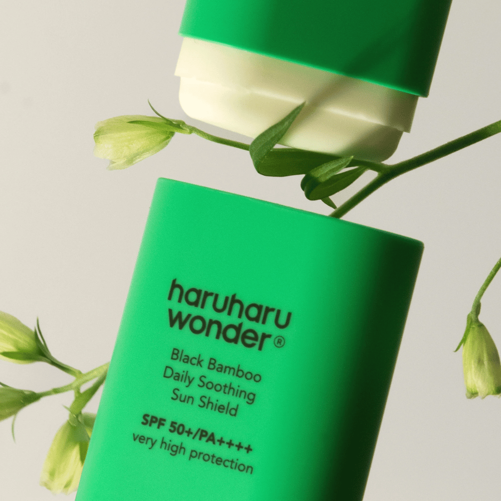 Gros plan de Haruharu Wonder Black Bamboo Daily Soothing Sun Shield – un écran solaire vert en format stick avec SPF 50+ PA++++, entouré de détails de plantes vertes.