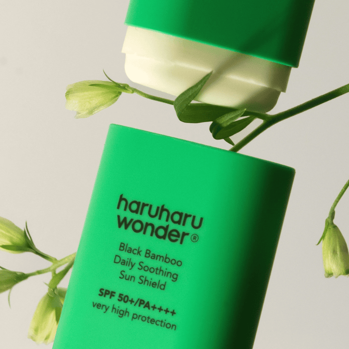 Gros plan de Haruharu Wonder Black Bamboo Daily Soothing Sun Shield – un écran solaire vert en format stick avec SPF 50+ PA++++, entouré de détails de plantes vertes.