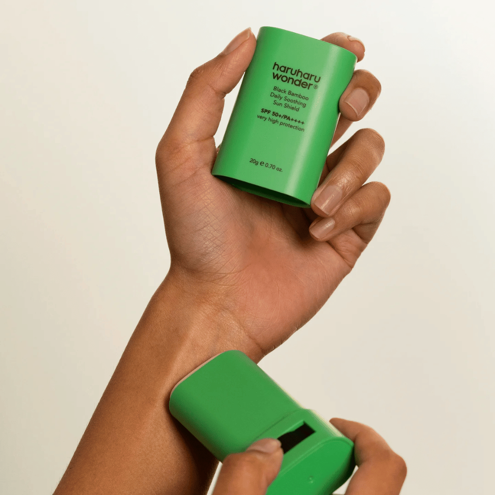 Une personne applique Haruharu Wonder Black Bamboo Daily Soothing Sun Shield – un bâton solaire vert avec SPF 50+ PA++++ – sur le poignet.