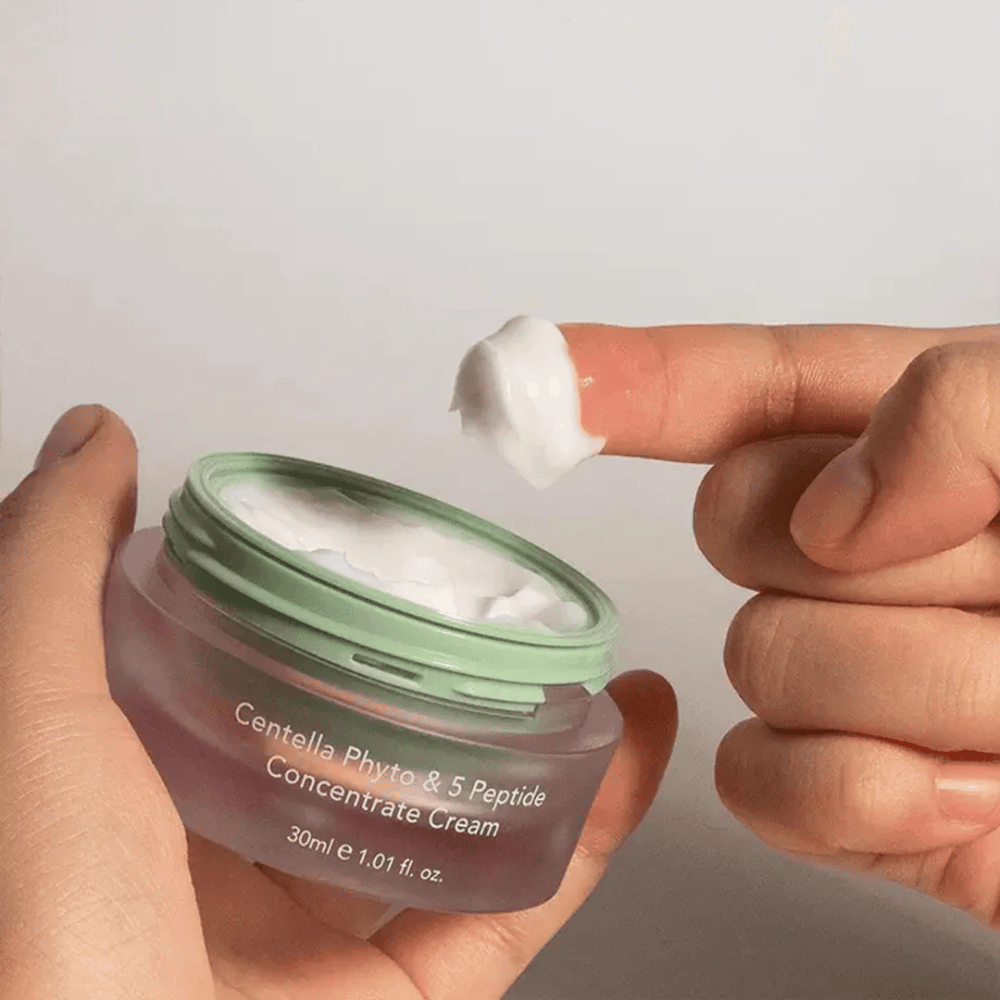 Main prenant une noisette de Centella Phyto & 5 Peptide Concentrate Cream dans un pot.