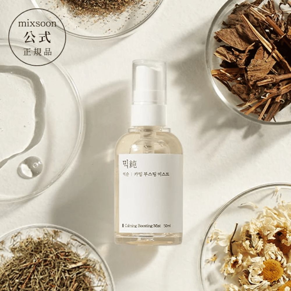Un flacon pulvérisateur transparent avec l'étiquette 'Calming Boosting Mist' de Mixsoon, entouré d'herbes séchées et de fleurs dans des bols blancs sur un fond beige, mettant en valeur les ingrédients naturels des produits.