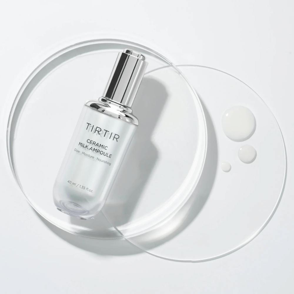 Une bouteille transparente TIRTIR Ceramic Milk Ampoule sur une plaque de verre avec des gouttes, contre un fond blanc, met en valeur l'éclat, l'hydratation et la nutrition.