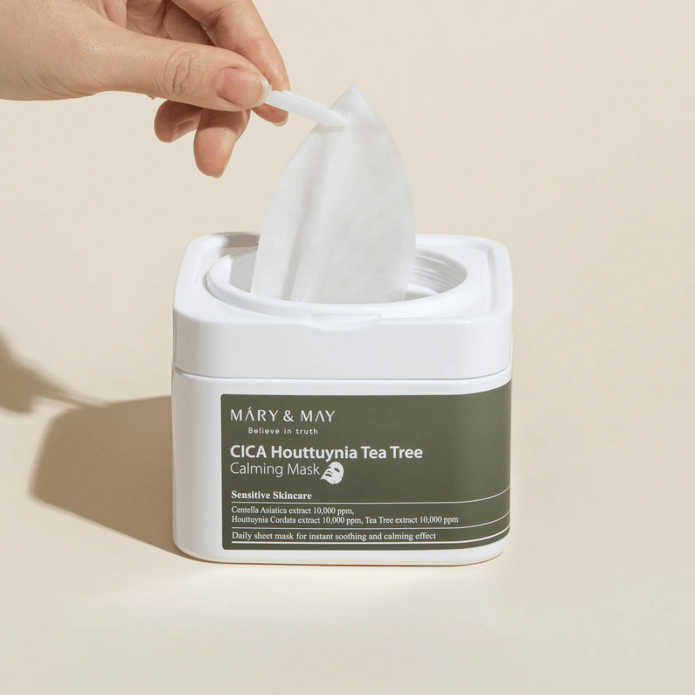 Main retirant un masque en feuille d'un pot Mary & May Cica Houttuynia Tea Tree Calming Mask – masque facial apaisant pour peau sensible avec Cica et extrait de Tea Tree.