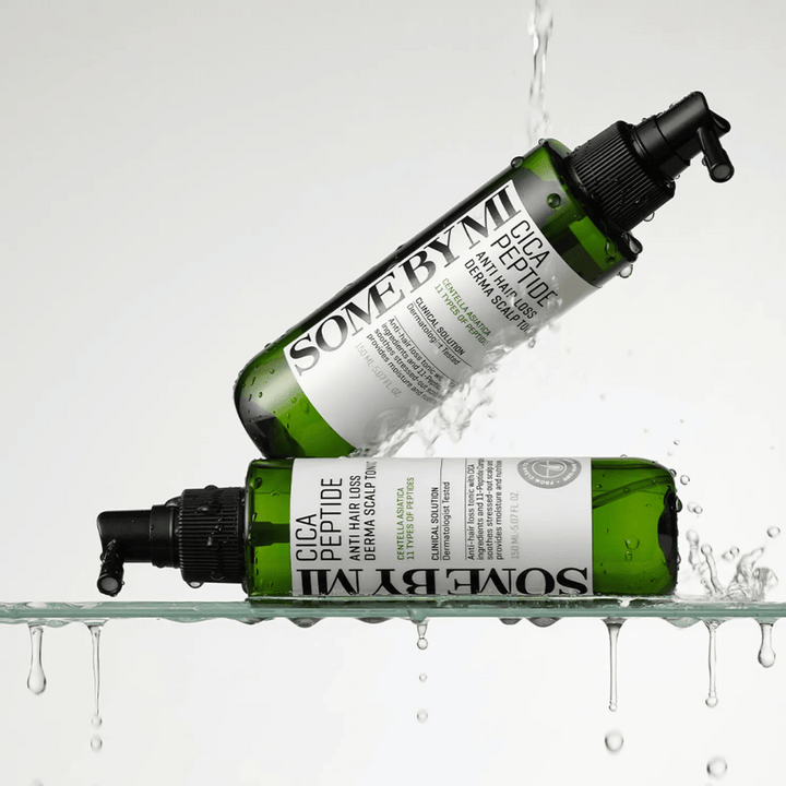 Deux bouteilles SOME BY MI Cica Peptide Anti Hair Loss Derma Scalp Tonic sont dans et au-dessus de l'eau avec des gouttes éclaboussant, bouteilles vertes avec un pulvérisateur noir et une étiquette blanche.