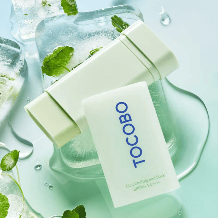 Tocobo Cica Cooling Sun Stick SPF50+ PA++++ sur des glaçons avec des feuilles de plantes vertes, transmettant une sensation rafraîchissante et revigorante.
