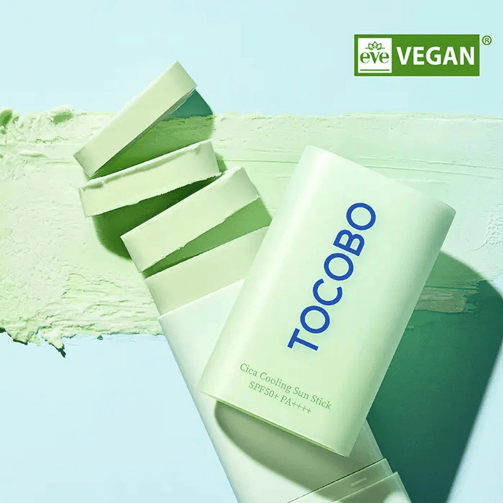 Tocobo Cica Cooling Sun Stick SPF50+ PA++++ dans un emballage vert clair avec label vegan (EVE VEGAN), posé sur une couche de stick solaire vert.