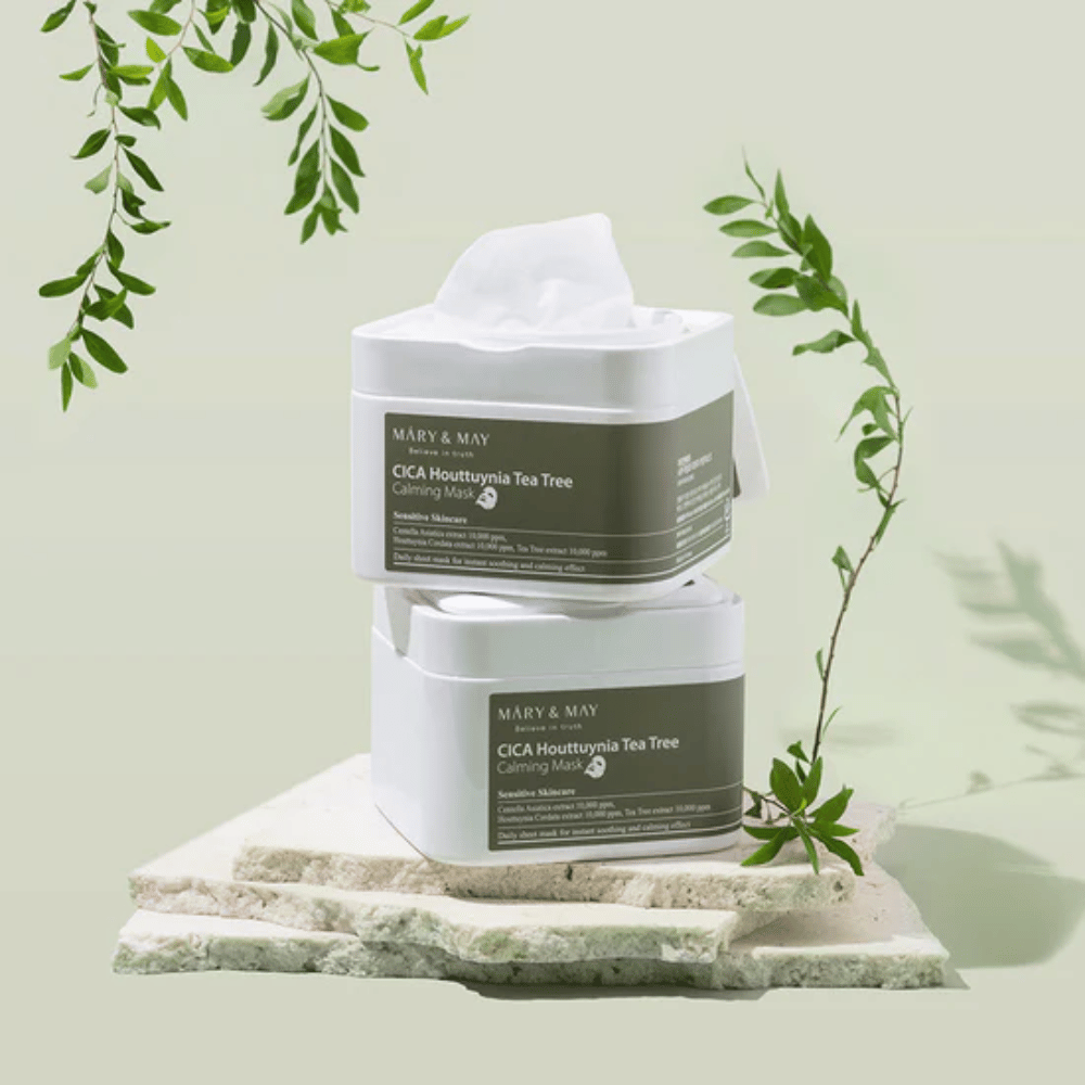 Deux pots Mary & May Cica Houttuynia Tea Tree Calming Mask placés sur une pierre naturelle avec des détails de plantes vertes – masques en feuille apaisants pour peau sensible.