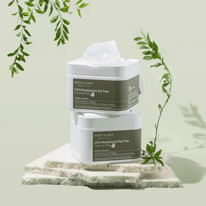 Deux pots Mary & May Cica Houttuynia Tea Tree Calming Mask placés sur une pierre naturelle avec des détails de plantes vertes – masques en feuille apaisants pour peau sensible.