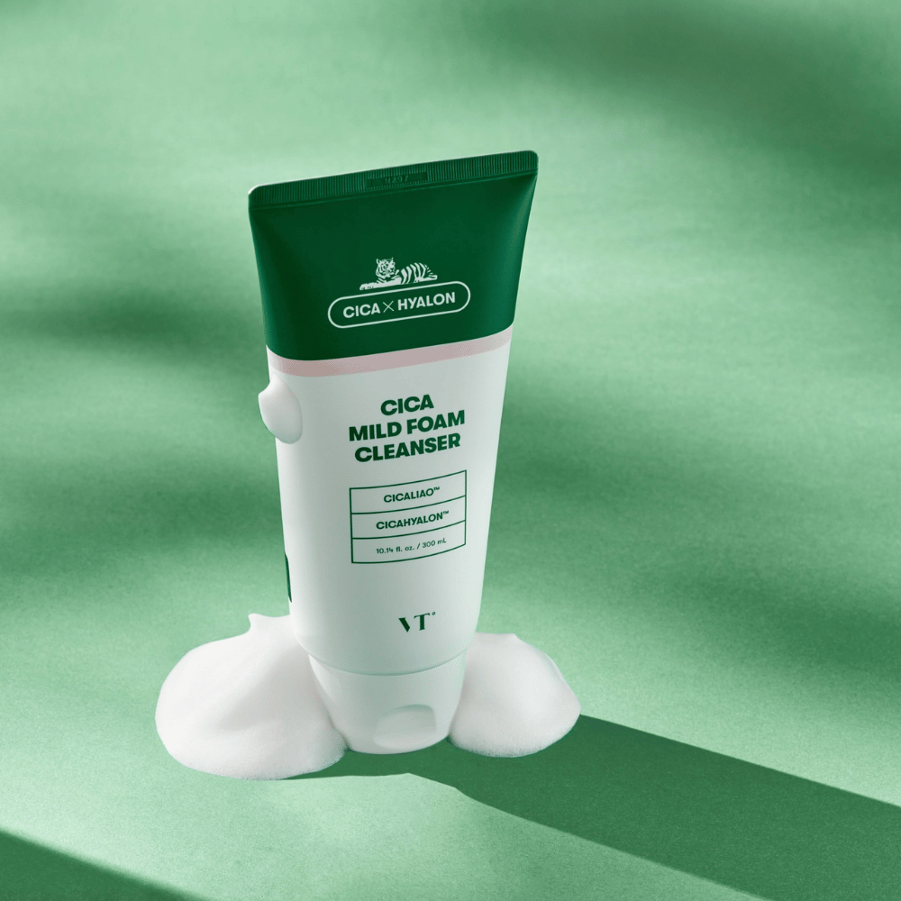 Tube avec VT Cica Mild Foam Cleanser debout sur un fond vert avec de la mousse autour de la base. Le produit a un design vert et blanc et est commercialisé avec CICALIAO™ et CICAHYALON™.