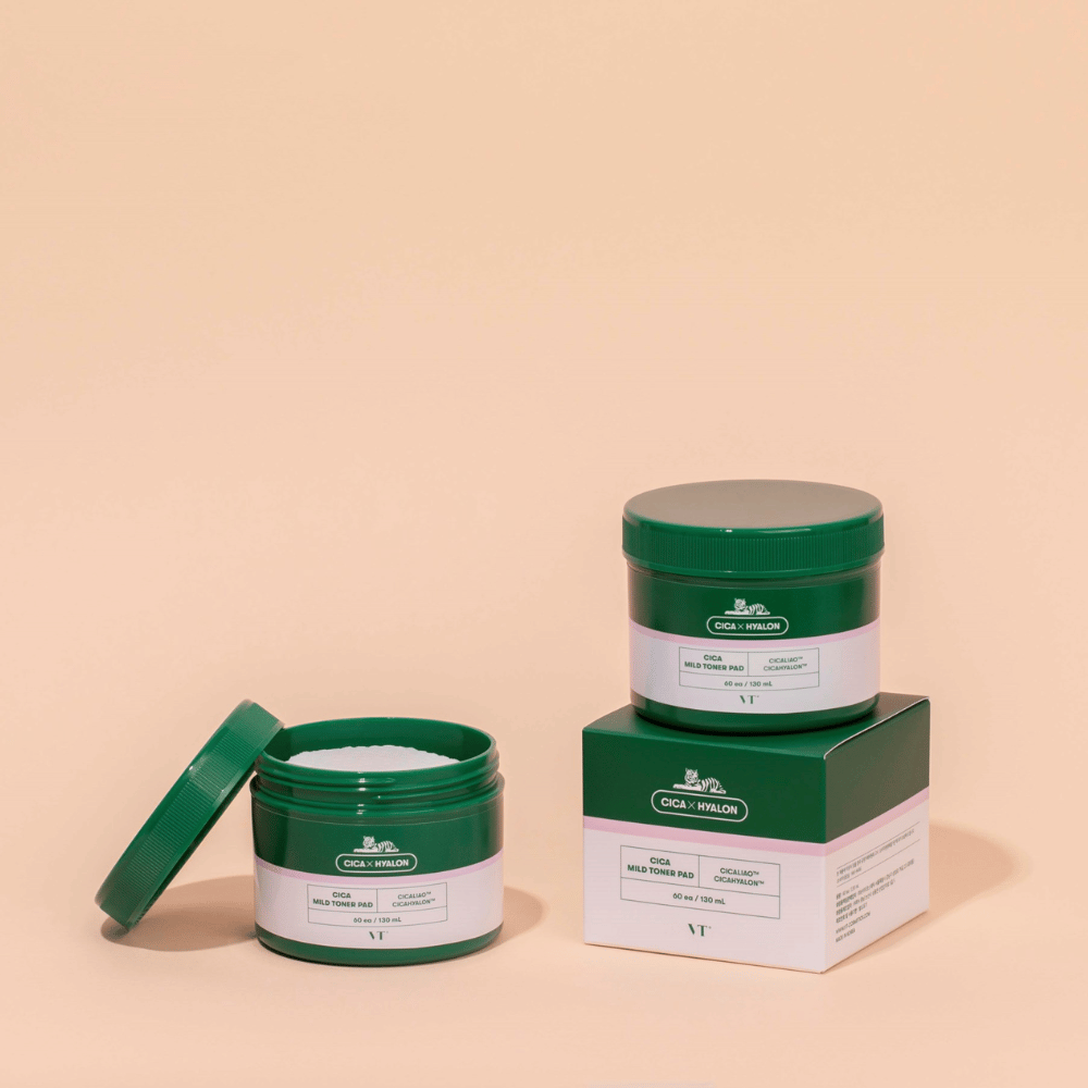 Deux pots verts avec VT Cica Mild Toner Pad, un ouvert montrant les tampons de toner blancs et un fermé placé sur son emballage de produit, sur fond beige.