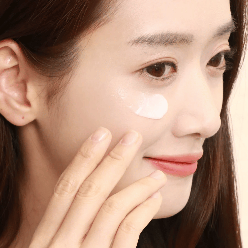 Une femme applique de la crème pour les yeux sous l'œil avec le bout des doigts - gros plan montrant comment le produit est doucement massé dans la peau pour l'hydratation et les soins.