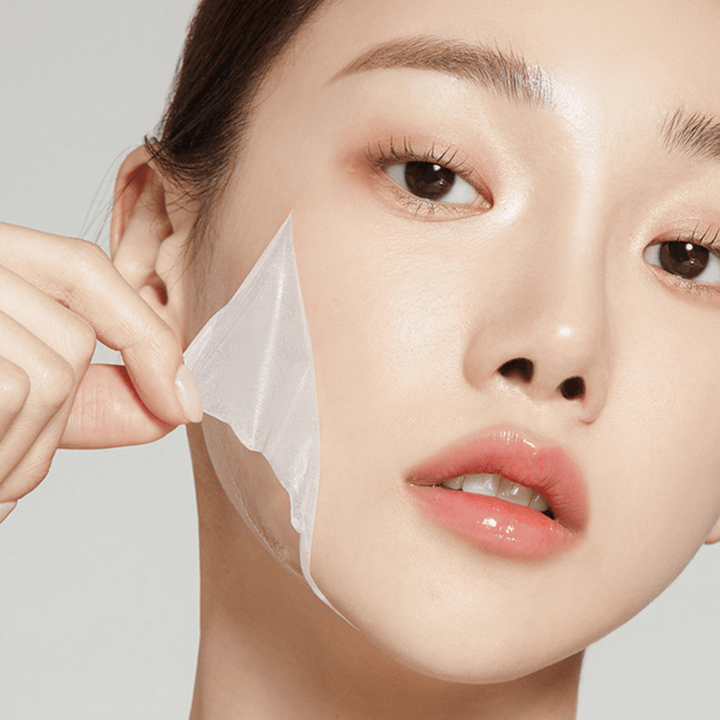 L'image montre une jeune femme en train de retirer un masque facial fin, mettant en valeur sa peau hydratée et douce. Le masque épouse les contours du visage, donnant l'impression d'un produit de soin de la peau efficace et doux. Son expression est détendue.