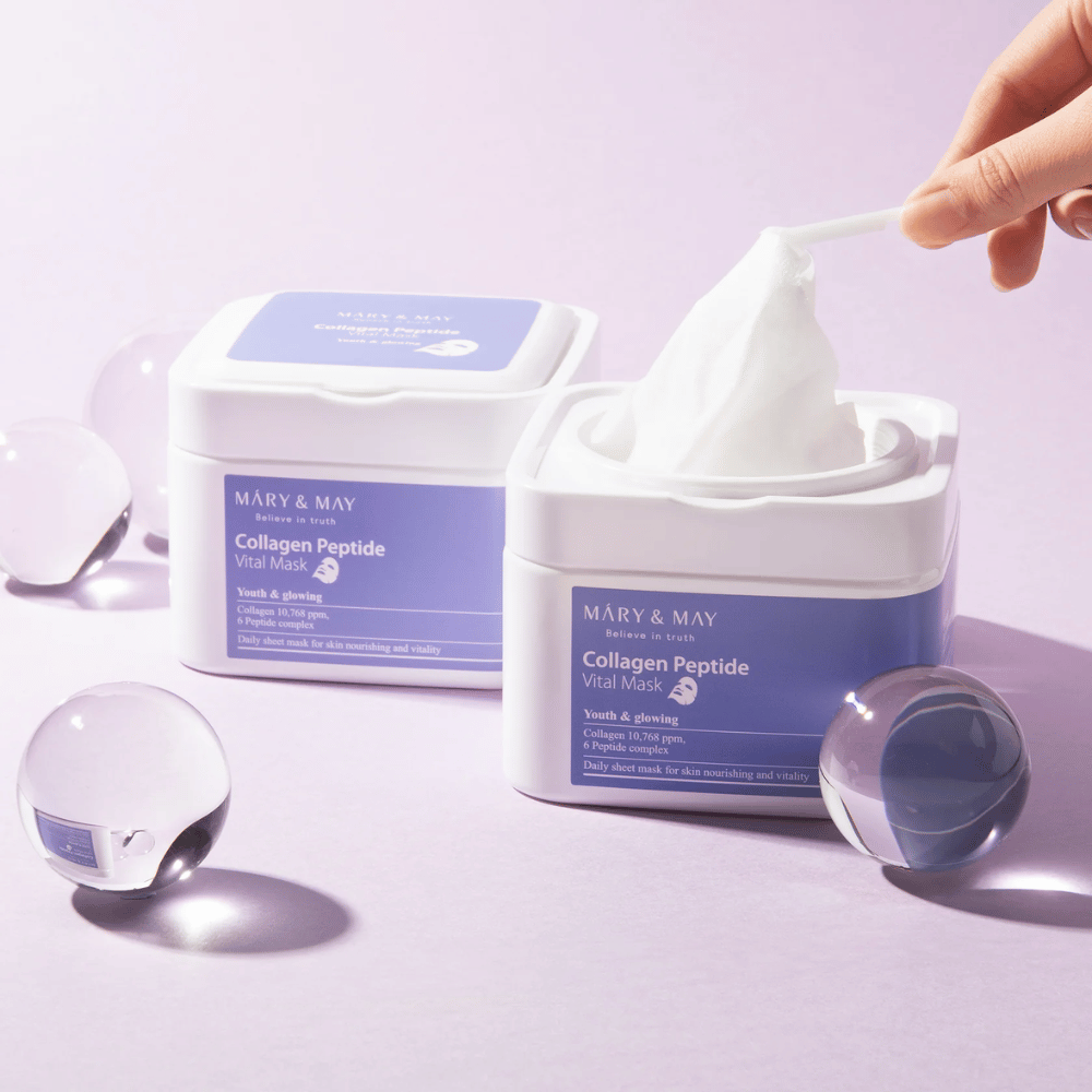 Une main prend un masque d'un pot de MARY & MAY Collagen Peptide Vital Mask. Le masque est destiné à un usage quotidien pour nourrir et illuminer la peau, avec du collagène et des peptides pour soutenir la jeunesse de la peau.