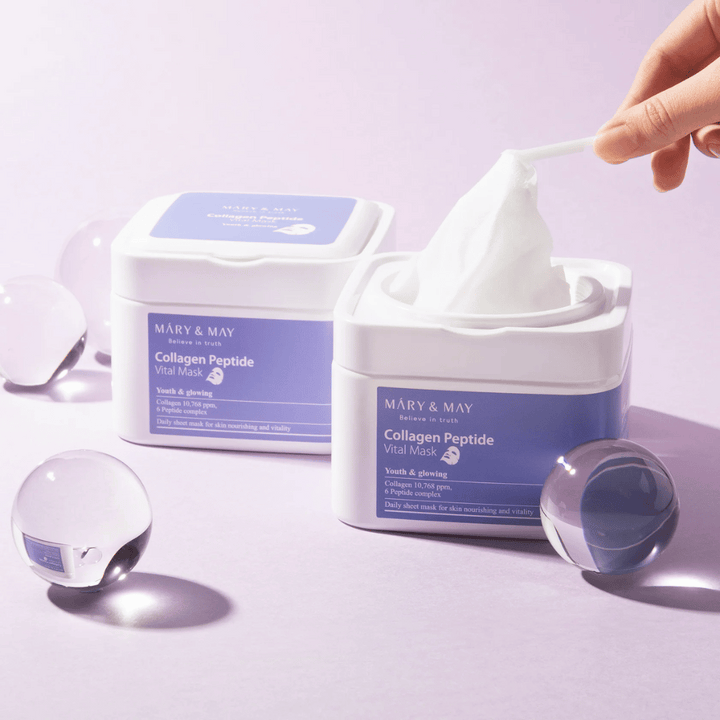 Une main prend un masque d'un pot de MARY & MAY Collagen Peptide Vital Mask. Le masque est destiné à un usage quotidien pour nourrir et illuminer la peau, avec du collagène et des peptides pour soutenir la jeunesse de la peau.