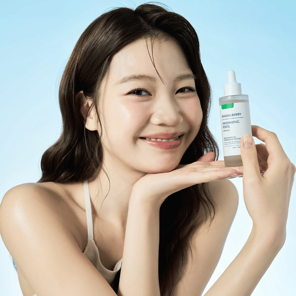 Femme souriante tenant Eqqualberry Swimming Pool Ampoule, un produit de soin hydratant, avec les deux mains sur un fond bleu clair.