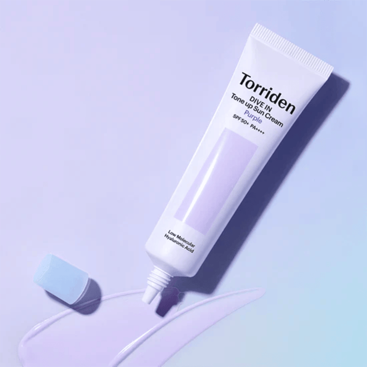 Tube ouvert de Torriden DIVE IN Tone Up Sun Cream Purple avec une texture de crème solaire teintée de violet qui montre la formule correctrice de couleur du produit.