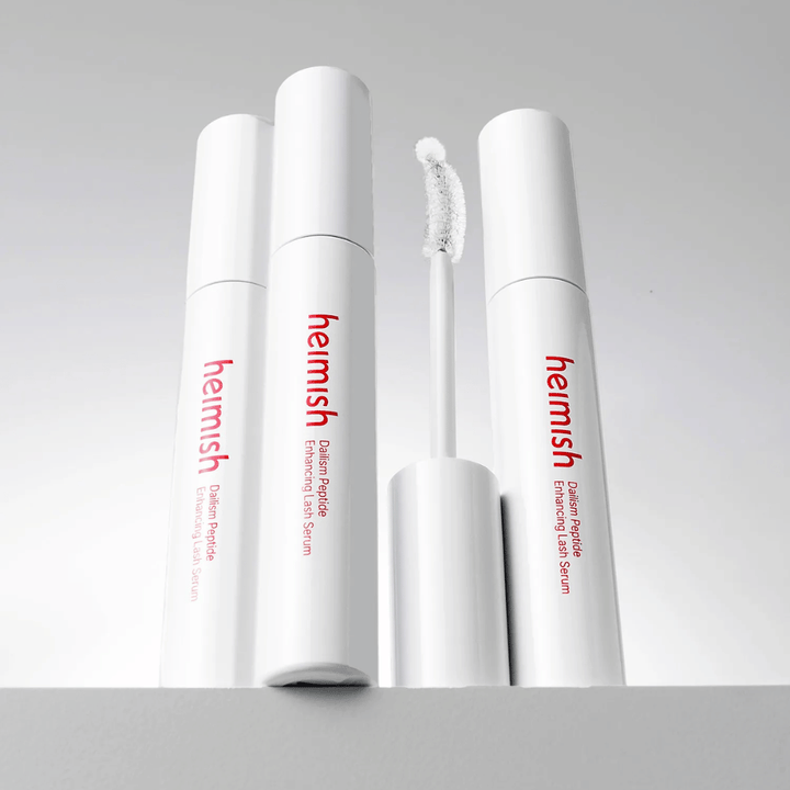 Plusieurs emballages de Heimish Dailism Peptide Enhancing Lash Serum sont présentés avec la brosse applicatrice incurvée. L’image met en valeur le design élégant du produit et sa brosse de précision pour une application facile.