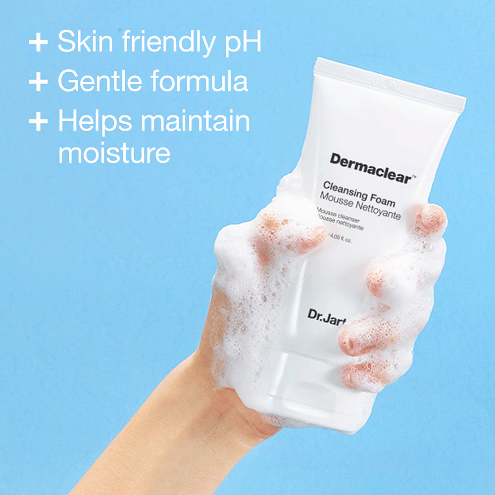 Main couverte de mousse tenant Dr.Jart+ Dermaclear Cleansing Foam sur fond bleu, avec texte soulignant le pH respectueux de la peau, la formule douce et les propriétés hydratantes.