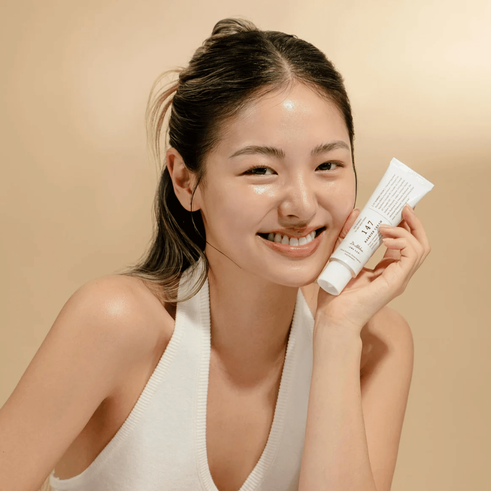 Modèle avec une peau éclatante souriant et tenant Dr. Althea 147 Barrier Cream – une crème pour le visage coréenne pour la barrière cutanée et l'hydratation.