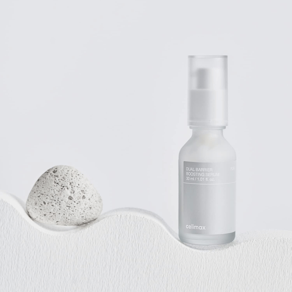 Celimax Dual Barrier Boosting Serum placé sur textile avec pierre, image de produit apaisante qui signale hydratation et barrière cutanée renforcée.
