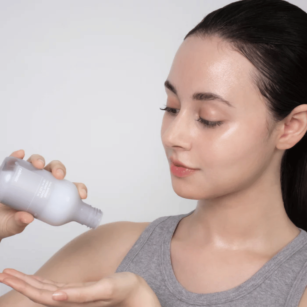 Femme avec une peau brillante et hydratée applique Celimax Dual Barrier Creamy Toner en versant le produit dans la paume de sa main avant sa routine de soins de la peau.